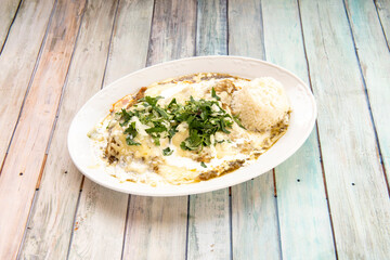 Mexican tray of green enchiladas with raw white rice, parsley, coriander and onion