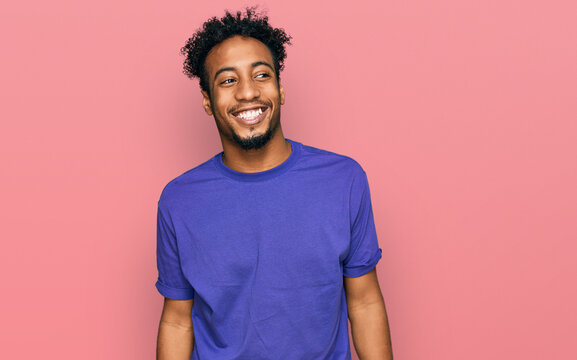 Young african american man with beard wearing casual purple t shirt looking away to side with smile on face, natural expression. laughing confident.