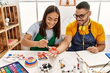 Young hispanic couple smiling happy painting hands sitting on the table at art studio.