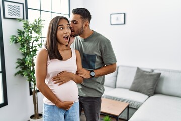 Fototapeta premium Young interracial couple expecting a baby, touching pregnant belly hand on mouth telling secret rumor, whispering malicious talk conversation