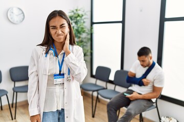 Fototapeta premium Young asian doctor woman at waiting room with a man with a broken arm touching mouth with hand with painful expression because of toothache or dental illness on teeth. dentist