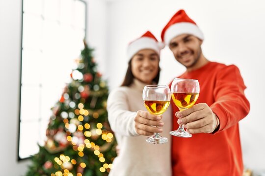 Young hispanic couple smiling happy toasting with champagne standing by christmas tree at home.