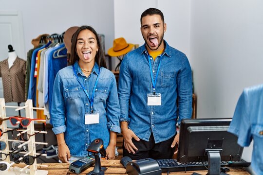 Young interracial people working at retail boutique sticking tongue out happy with funny expression. emotion concept.