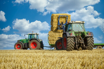 Fototapeta na wymiar Strohernte - Traktor mit Frontlader beim Beladen eines Transportanhängers mit Strohballen.