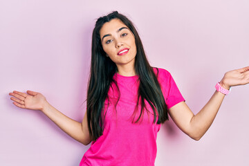 Young hispanic girl wearing casual pink t shirt clueless and confused expression with arms and...