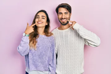 Young hispanic couple wearing casual clothes smiling cheerful showing and pointing with fingers teeth and mouth. dental health concept.