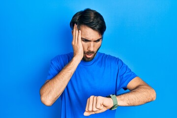 Naklejka premium Young hispanic man wearing casual clothes looking at the watch time worried, afraid of getting late