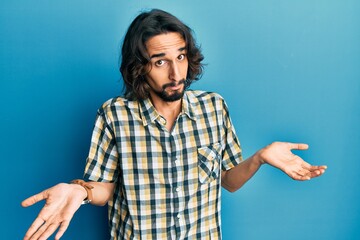 Young hispanic man wearing casual clothes clueless and confused expression with arms and hands...