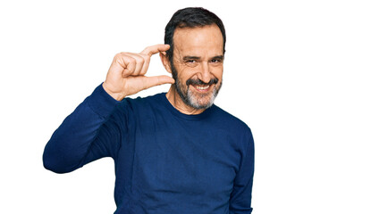 Middle age hispanic man wearing casual clothes smiling and confident gesturing with hand doing small size sign with fingers looking and the camera. measure concept.