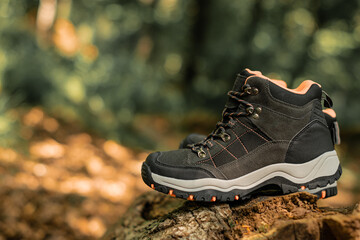 Closeup on pair of dark grey hiking boots on a natural raw wood in the woodland. Selective focus on dark shoes with ankle support for walking, surrounded by nature.
