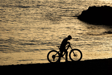 Fototapeta premium Silhouette of a boy pushing the bike on beach with the ocean in background