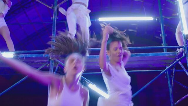 Many female dancers dressed in white shorts dancing inside abandoned building in high scaffolding construction . Stylish Girls dancing, twerking , doing gymnastic movements , jumping . Slow motion 
