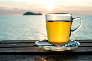 Cup of green tea front of at sunset light on wooden tabletop. Sea view