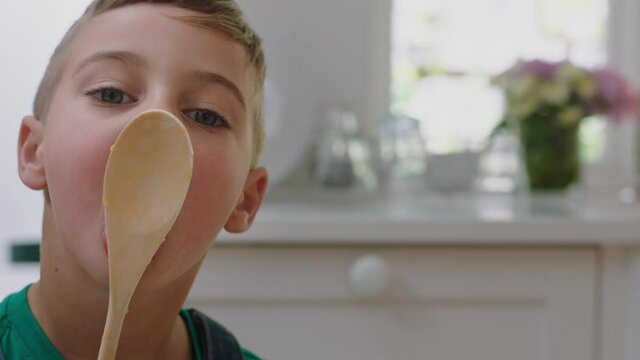 happy little boy tasting delicious chocolate pudding using spoon enjoying homemade treats in kitchen