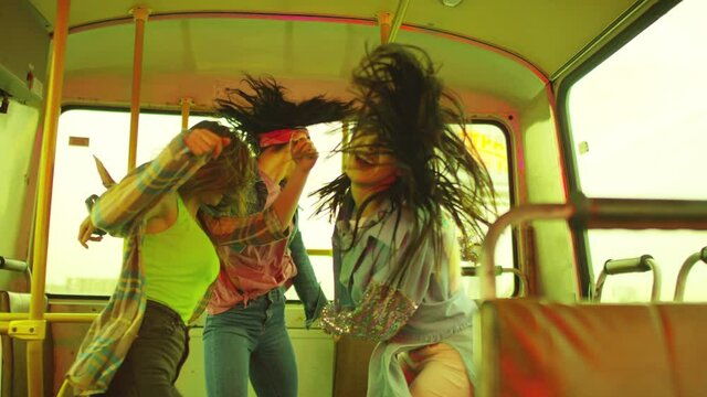 Three young beautiful and happy blogger girls dancing , moving , having fun inside public transport .  Stylish girls in sport outfit jumping whirling and shaking body inside auto bus in slow motion . 