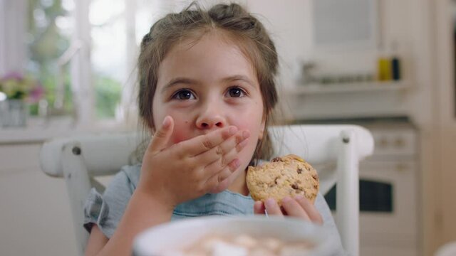 cute little girl eating cookie dipping biscuit into hot chocolate enjoying delicious treat at home in kitchen