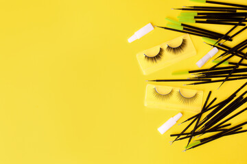 Different tools for eye lash extension on trendy bright yellow background. Fake eyelashes, brushes...