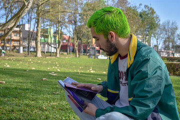Hombre joven sentado leyendo revista o libro con barba y cabello verde neón alternativo sobre el...