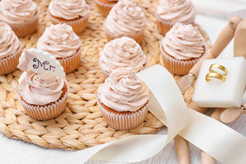 Wooden mannequin with wedding rings and tasty cupcakes on light background