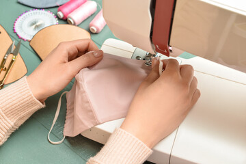 Woman sewing medical mask on color wooden background