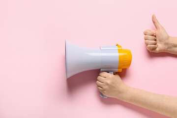 Woman with megaphone showing thumb-up on color background