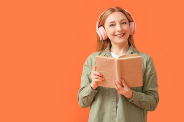 Mature woman with headphones reading book on color background