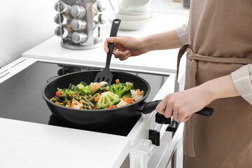 Woman frying vegetables on stove in kitchen