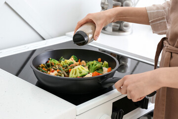 Woman frying vegetables on stove in kitchen, closeup