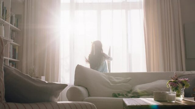 happy little girl opening curtains looking out window at beautiful new day with bright sunlight playful child feeling positive about future