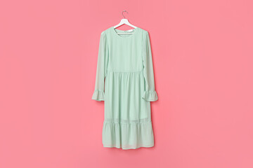 Hanger with stylish female dress on color background