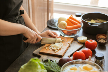 Young woman cutting onion for delicious borscht on wooden board in kitchen