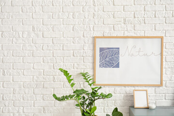 Stylish workplace with blank photo frame and modern picture with word NATURE on white brick wall