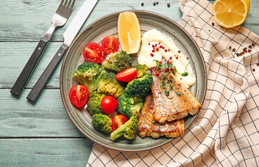Plate with tasty baked cod fillet and vegetables on color wooden background
