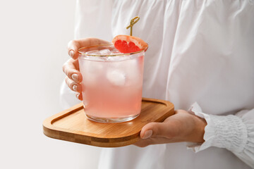 Woman holding glass of tasty grapefruit margarita on light background, closeup