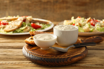 Bowls of tasty Caesar sauce and croutons on wooden background