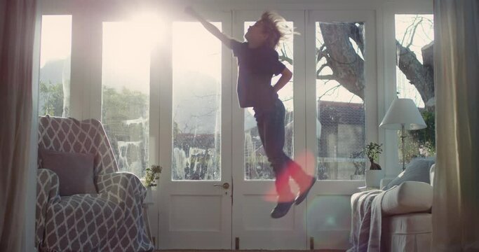happy little boy jumping off sofa having fun playing game of pretend child in playful mood enjoying weekend morning at home with sunlight shining through window childhood imagination 4k footage