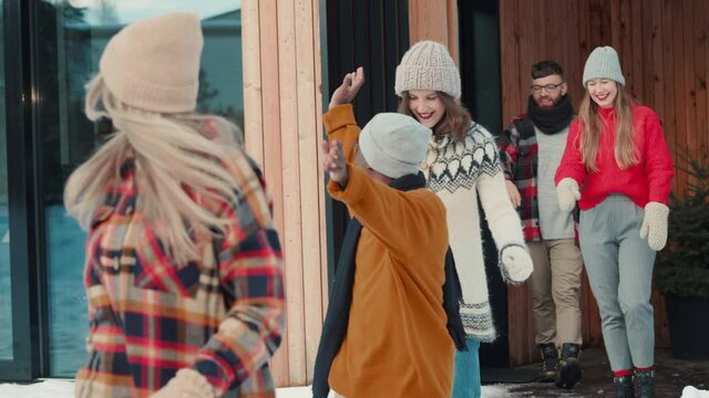 CHRISTMAS PARTY Happy young smiling friends get inside red car hugging, waving goodbye at snowy winter house slow motion