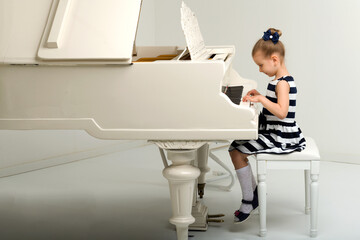 Side view of cute little girl playing grand piano