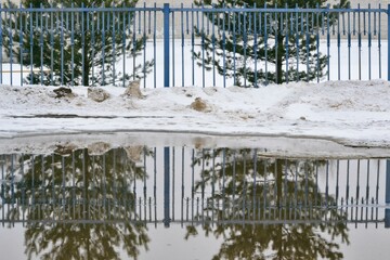 A road with melting snow, puddles and ice on a cloudy spring day. Reflections in cold water. Snow...