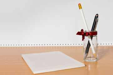 A neat picture of task pad notebook and two pens in glass with red ribbon.