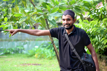 A young man is standing with his one hand outstretched and smiling