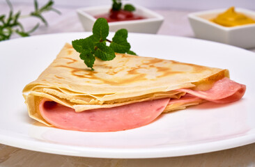 french crepe with pork ham and mozzarella cheese on a white plate with a mint leaf on top, served with ketchup and mustard on a marble surface. fancy concept. close up view