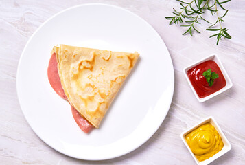 pork ham and mozzarella cheese crepe on a white plate, served with ketchup and mustard on a marble surface. elegant restaurant concept. copy space for advertising. top view