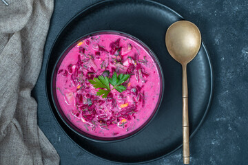 Delicious cold summer beetroot soup with cucumber, boiled egg, radish in black bowl on table