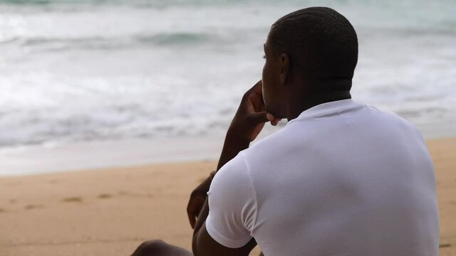 Afro American sporty man sitting on the beach and looks at the sea 