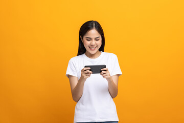 Naklejka premium Excited Beautiful young asian women play mobile game and standing on isolated yellow background. Playing game on smartphone winning victory moment. Very enjoy and fun relax time