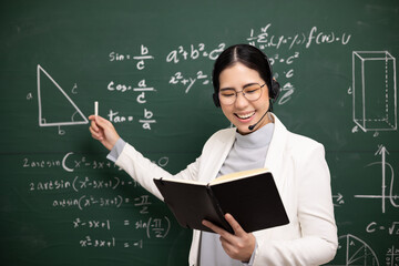 Young asian teacher woman teaching holding book and chalk video conference with student looking camera. Female teacher training the mathematics in classroom blackboard from online course.