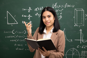 Young asian teacher woman teaching holding book and video conference with student looking camera. Female teacher training the mathematics in classroom blackboard from online course.