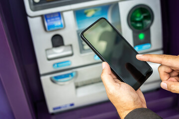 Young businessman standing front of atm machine using smartphone withdraw the money without atm...