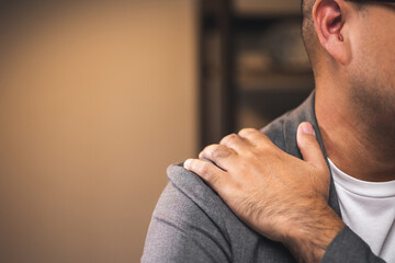 Fototapeta premium Young businessman works late at night in a dimly lit room. He tired and stressed needs rest. He has shoulder neck and back pain. Working hard and overtime too much going to symptom office syndrome.
